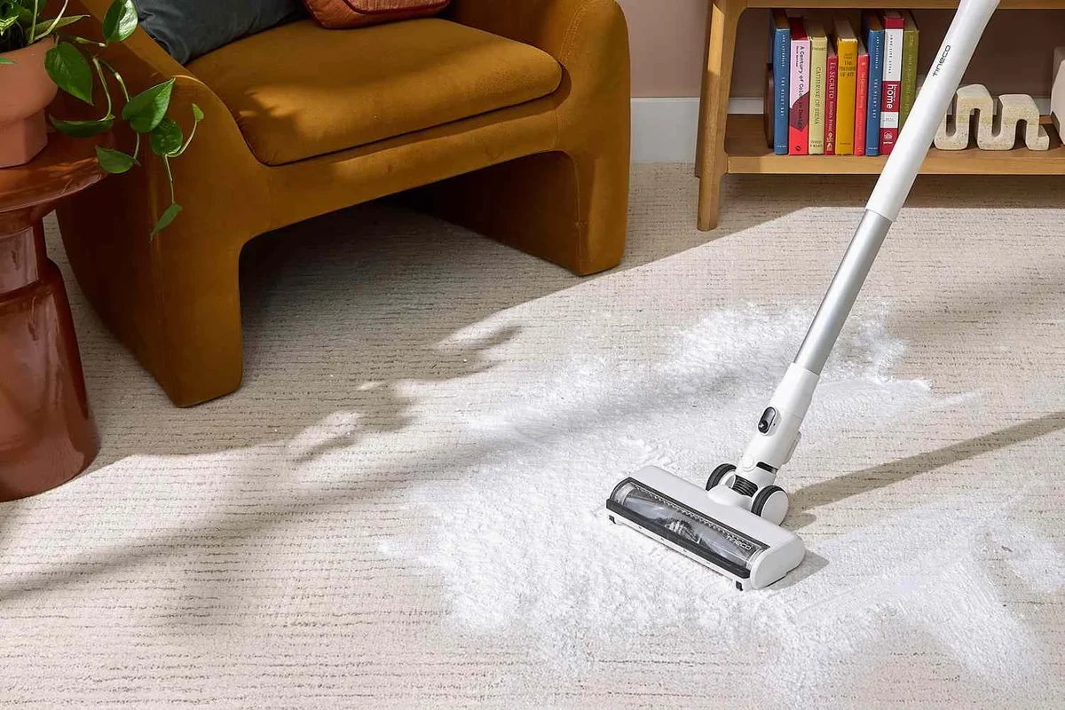 Baking soda sprinkled on a carpet stain beside a vacuum and cleaning cloth