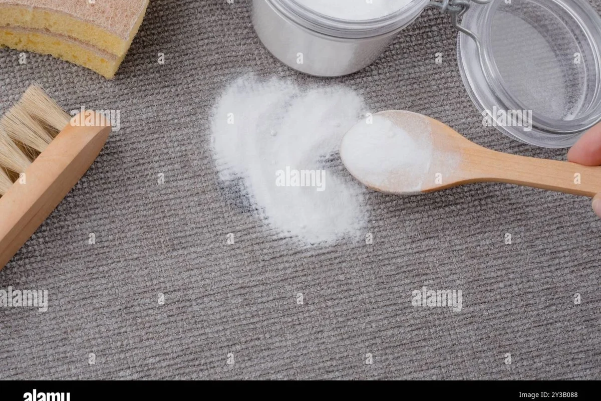Baking soda paste being used to treat an ink stain on fabric beside cleaning cloths