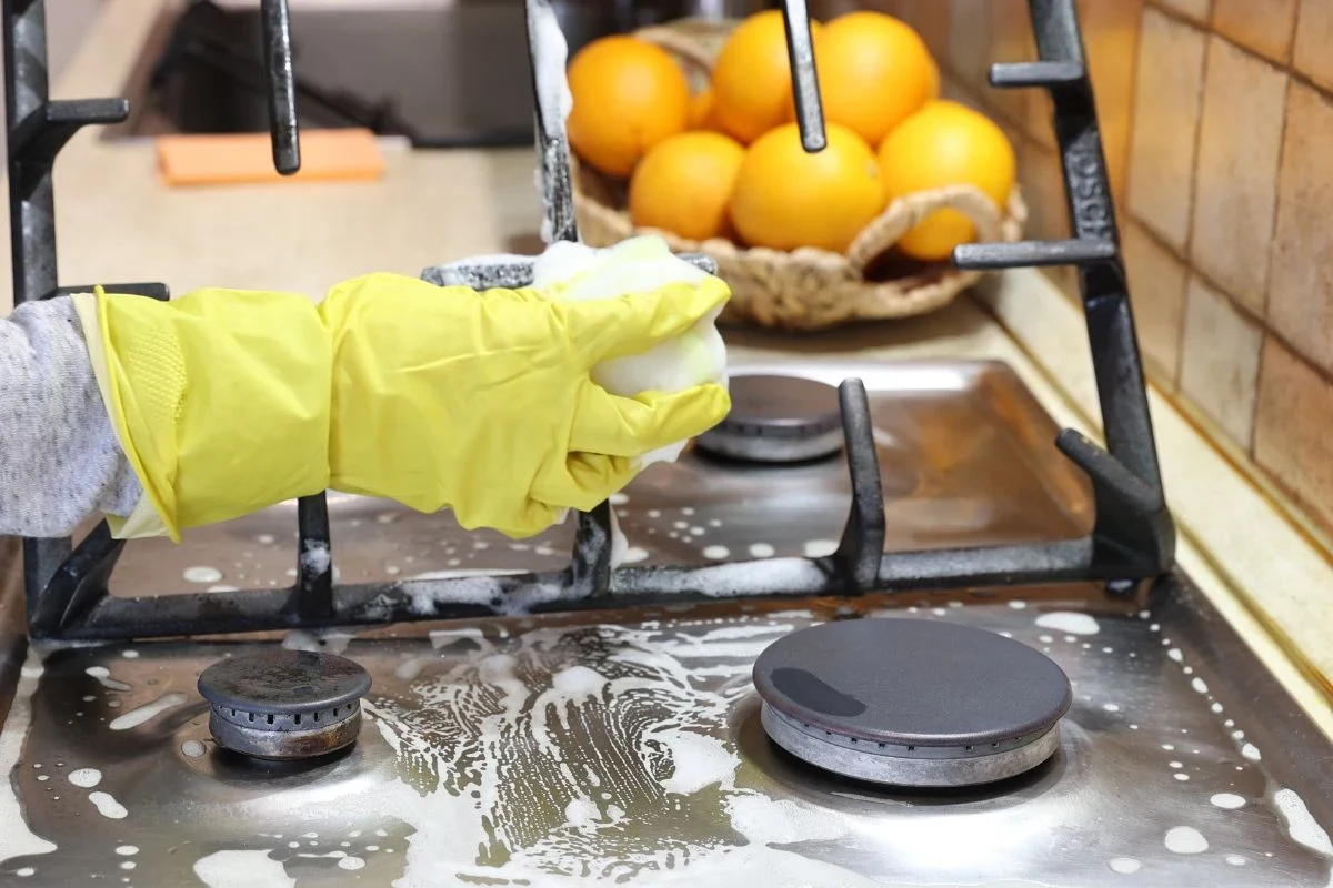 Person cleaning a stove surface with baking soda paste and a microfiber cloth