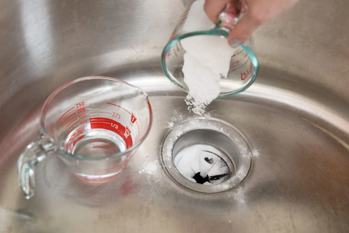 Garbage disposal cleaning with baking soda and vinegar beside a kitchen sink