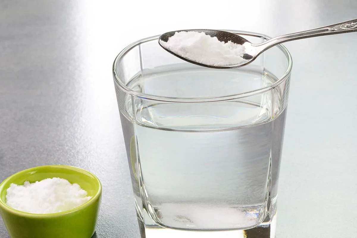 Glass of baking soda water on a kitchen counter with measuring spoon and baking soda jar