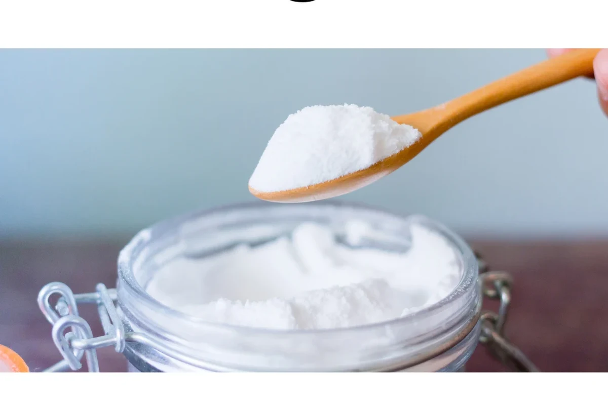 Glass of baking soda water beside a measuring spoon on a kitchen counter