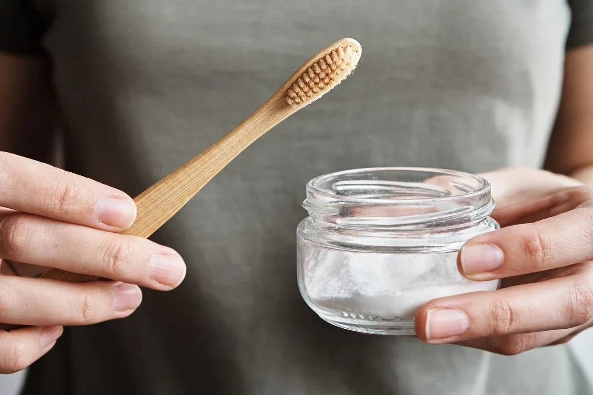 Person brushing teeth with a baking soda paste in a bathroom sink