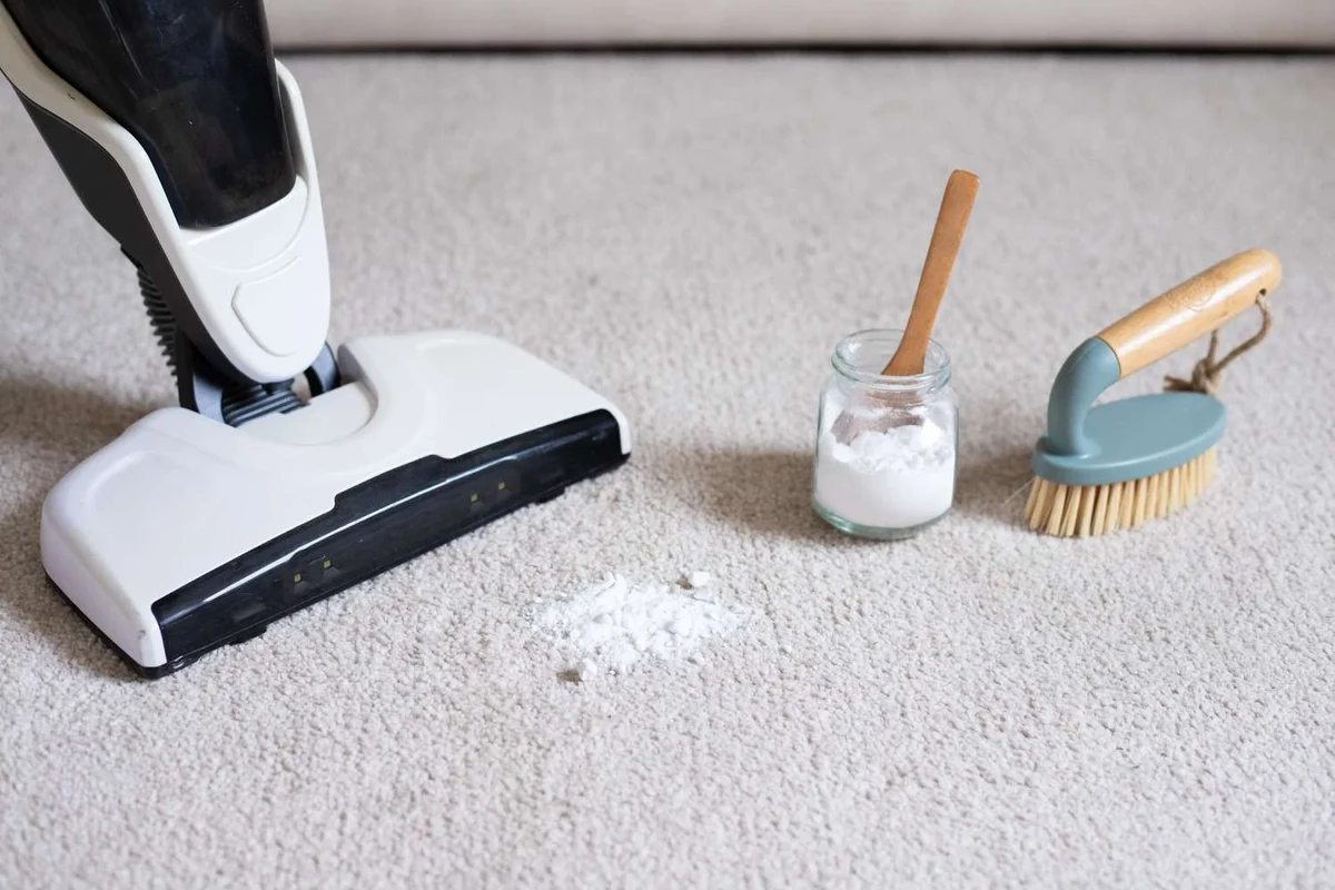 Baking soda sprinkled on carpet beside a vacuum for deodorizing