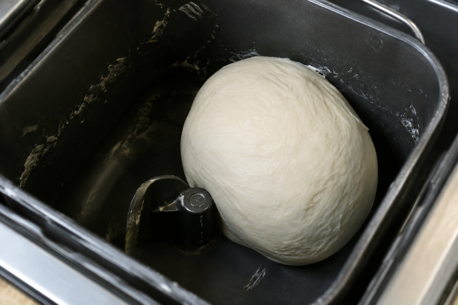 Close-up of bread dough forming a smooth ball in a bread machine pan